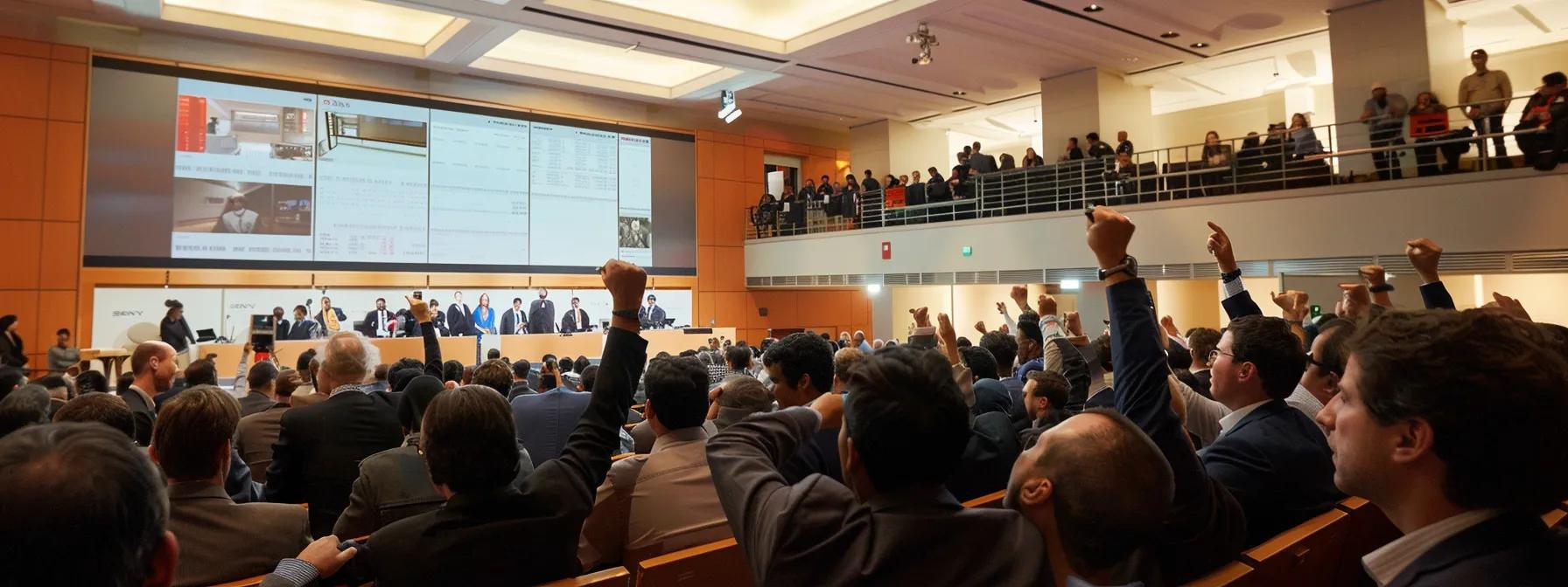 Auction scene with attendees raising hands to bid, large screen displaying auction details, and auctioneers at the front, illustrating what homeowners should do when facing foreclosure in Winston Salem.